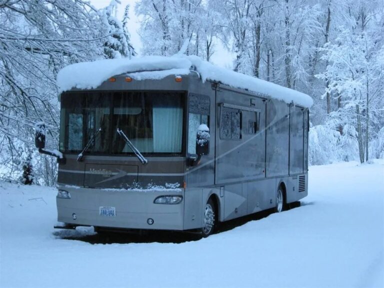 Class A motorhome covered in fresh snow among birch trees
